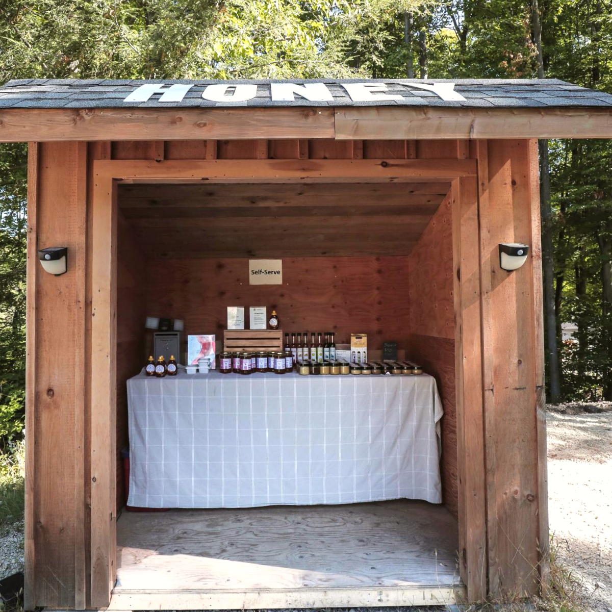 Self serve stand that says "Honey" on the roof. Inside is a table with honey products.