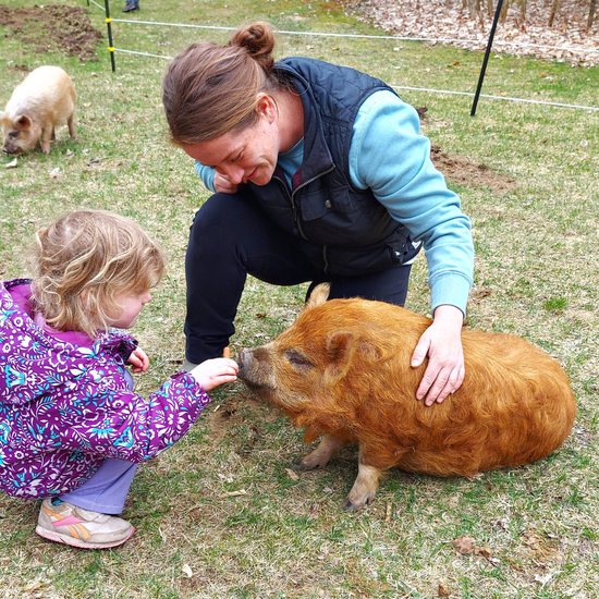 Mother and young daughter with a small KuneKune pig.