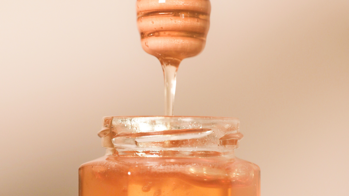 Honey dipper drizzling honey into a honey jar. 