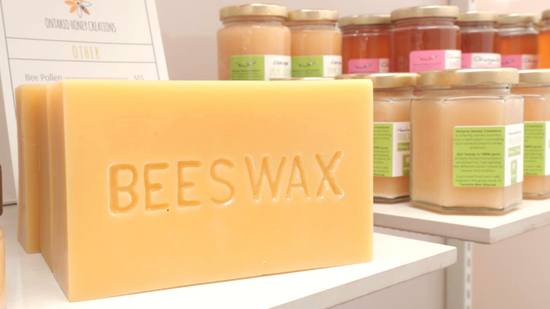 Block of yellow beeswax with the word "beeswax" imprinted on it. In the background is jars of honey.