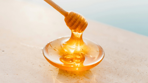 A wooden honey dipper drizzling honey into a bowl