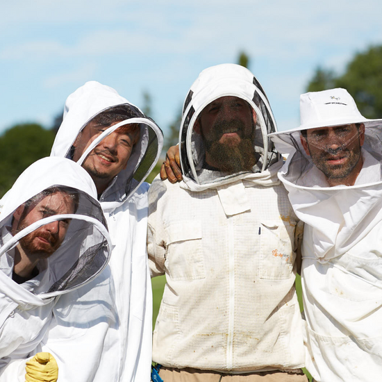 Four people, smiling, dressed in beekeeping suits.